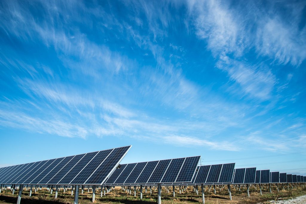 A field of solar panels producing renewable energy for the UK amongst some sunny skies with light clouds