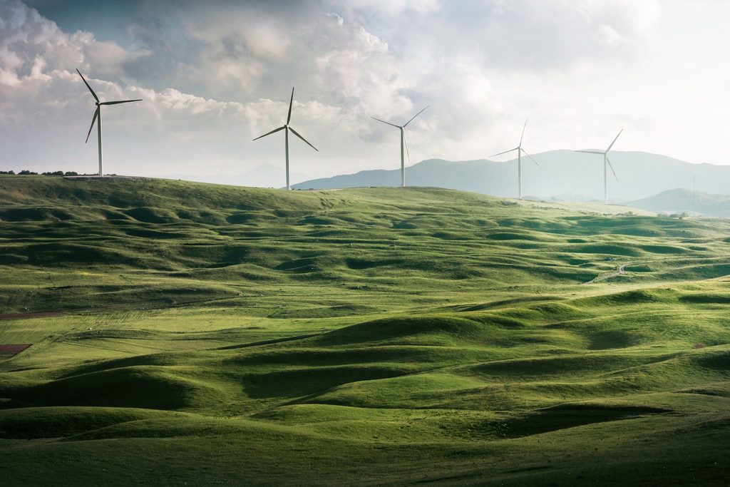 Wind turbines producing renewable energy for the UK set the backdrop of mountains with green, rolling hills in the foreground