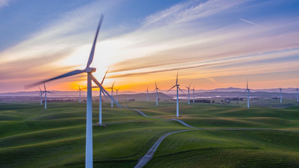 A field of wind turbines producing renewable energy for the UK against the background of an orange and pink sunset