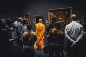 A monk stands out in the crowd at a museum, wearing bright yellow robes