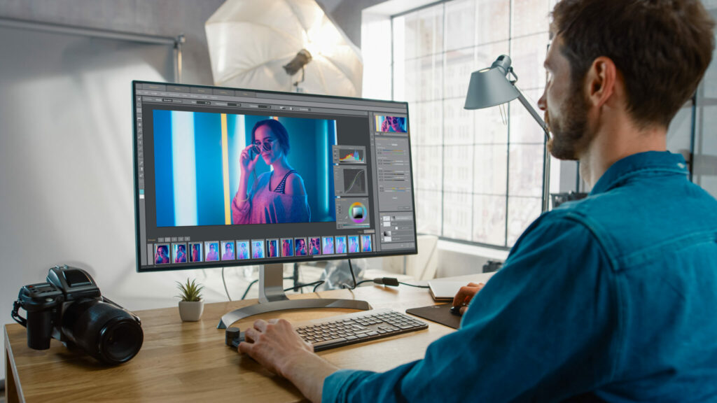 Professional Photographer Sitting at His Desk Uses Desktop Computer in a Photo Studio Retouches. After Photoshoot He Retouches Photographs of Beautiful Female Model in an Image Editing Software