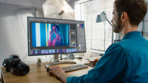 Professional Photographer Sitting at His Desk Uses Desktop Computer in a Photo Studio Retouches. After Photoshoot He Retouches Photographs of Beautiful Female Model in an Image Editing Software