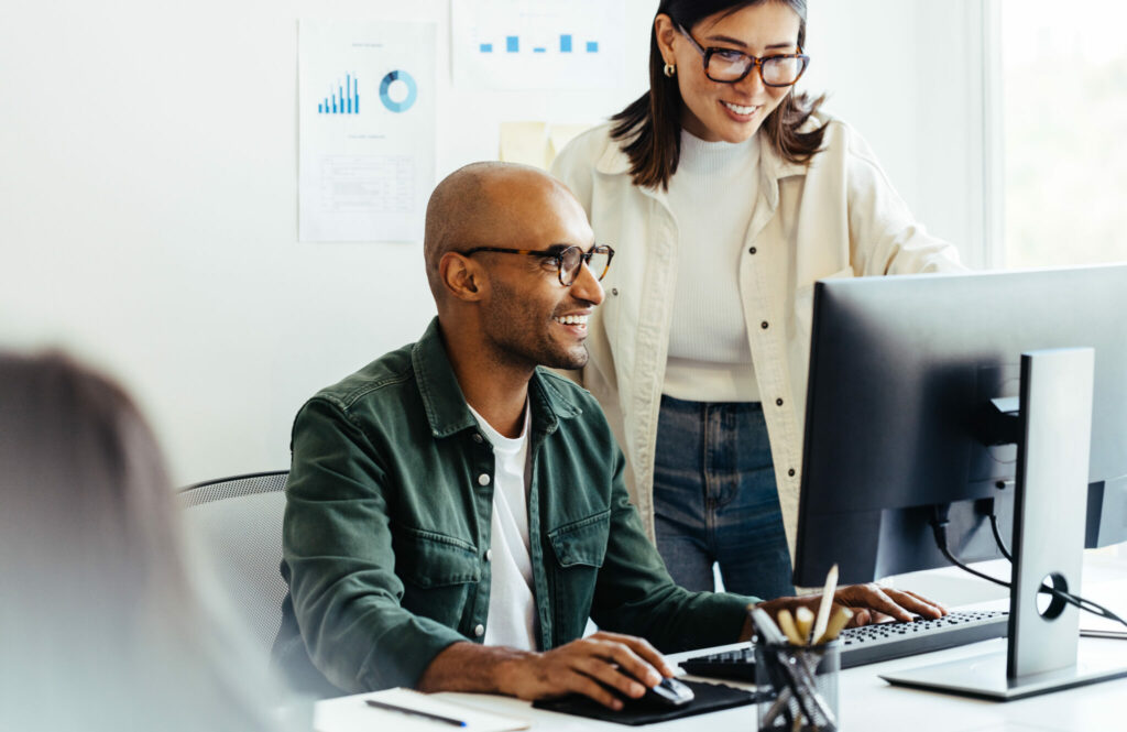 Web developers using a computer together in a creative office. Two business people working on a new ai marketing software developing project in an office.